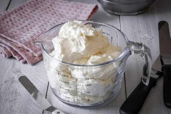 Ein Messbecher gefüllt mit luftiger Swiss Meringue Buttercreme, bereit für süße Kreationen.