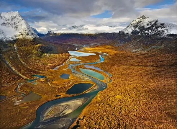 Herbstliche Farben im Tal mit Fluss und Seen, ideal für fernwanderwege schweden. Schneebedeckte Berge im Hintergrund.