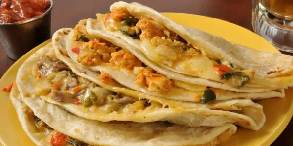 Quesadillas de pollo apiladas, rellenas de queso derretido y trozos de pollo sazonado, servidas en un plato amarillo con salsa al lado.