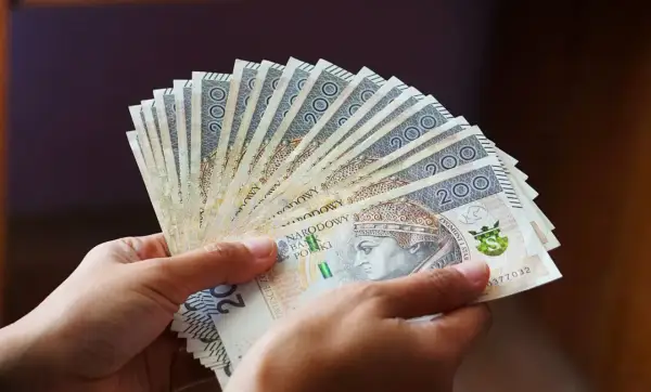 Dłonie trzymają wachlarz banknotów 200 zł. Pieniądze symbolizują świadczenie wspierające, które trafi do potrzebujących.