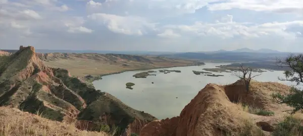 Paisaje de barrancos ocres y un lago sereno, ideal para una ruta de senderismo.