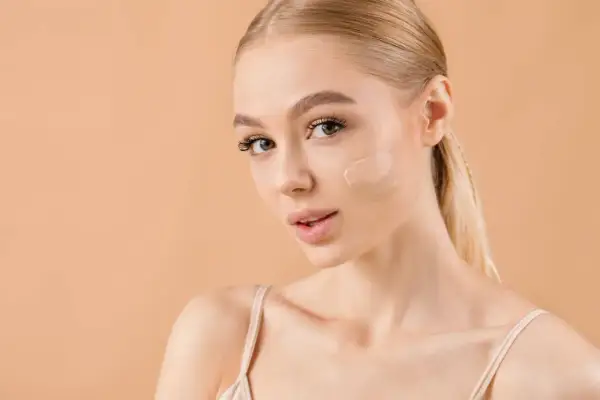 Kobieta z blond włosami pokazuje, gdzie nakładać korektor na policzek. Idealny odcień dla promiennej cery.