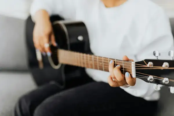 Dłoń z niebieskim lakierem na paznokciach gra na czarnej gitarze, tworząc rytmy w stylu reggae.