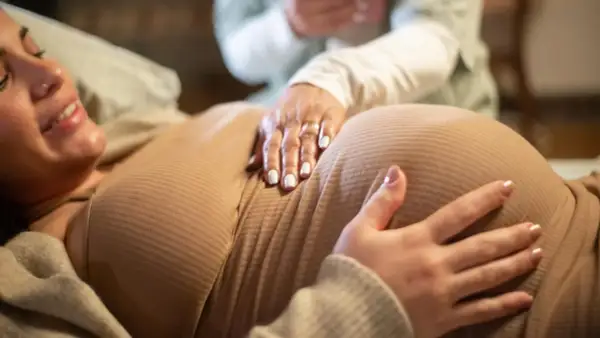 Manos sobre el vientre de una mujer embarazada, quizás consultando una tabla de contracciones de parto.
