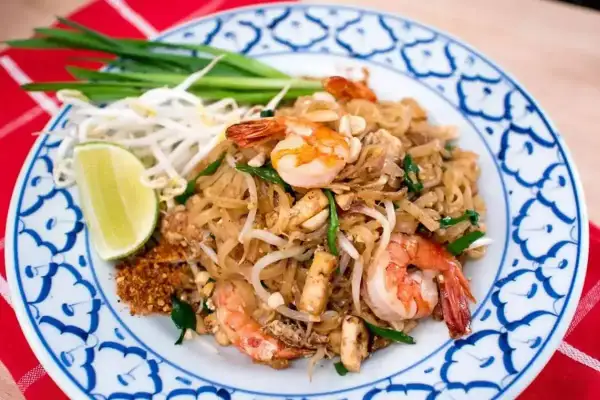 En tallrik med pad thai med räkor, böngroddar, lime och gröna lökar. En klassisk thailändsk rätt.