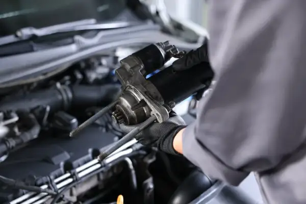 Mechanik w rękawiczkach trzyma rozrusznik. Zastanawiasz się, ile kosztuje wymiana rozrusznika?