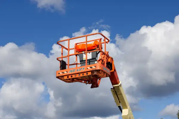 En orange korg från en JLG-lift mot en blå himmel med moln. Säkerhetsanvisningar för mobil arbetsplattform regler är synliga.