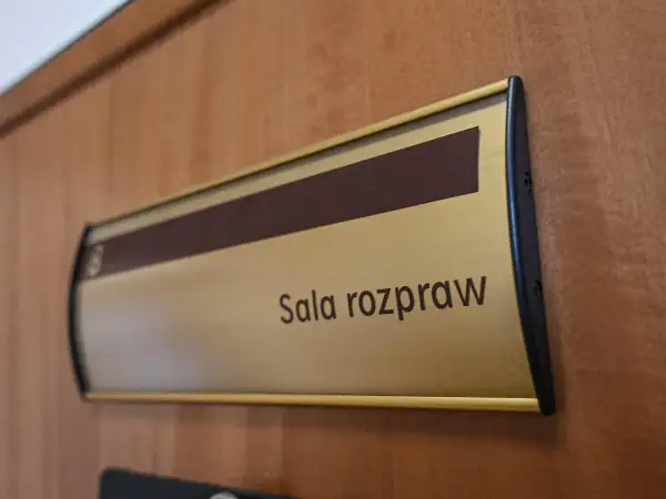 Tabliczka "Sala rozpraw" na drewnianych drzwiach. Może tu pracować referendarz sądowy.