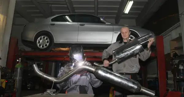 Mechanik w masce spawalniczej wykonuje spawanie wydechu. Obok stoi kolega z gotową częścią.