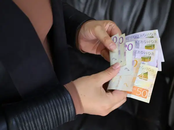 Ręce trzymają banknoty. Czy to sek, jaka to waluta? Widoczne są napisy "KRONOR" i cyfry 20, 50.