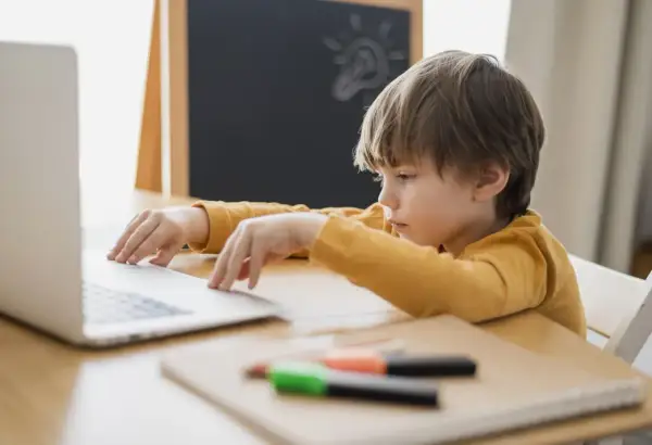 Chłopiec z problemami z koncentracją u dziecka siedzi przy laptopie, zamyślony. Na tablicy rysunek żarówki.