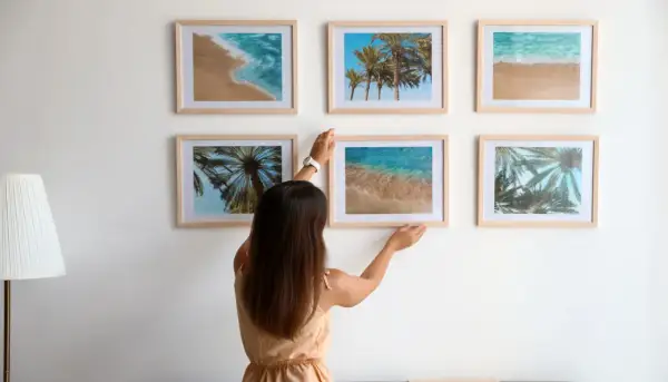Frau arrangiert Bilder mit Strandmotiven. Tolle bilder anordnen ideen für eine sommerliche Wandgestaltung.