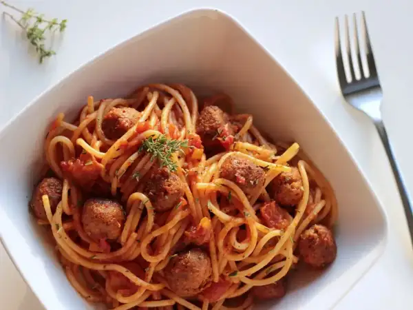 Spaghetti z klopsikami w sosie pomidorowym, udekorowane gałązką tymianku.