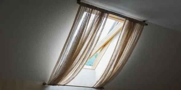 Voilage léger sur un montage store Velux ancien modèle, laissant passer la lumière du jour.
