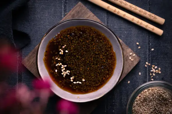 Schale mit Teriyaki-Sauce und Sesam, daneben Stäbchen und ein Glas Sesamsamen. Perfekt für dein Teriyaki Sauce Rezept!