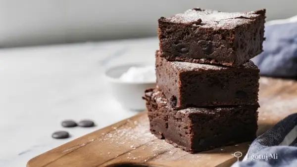 Pyszne, wilgotne brownie z kawałkami czekolady, posypane cukrem pudrem. Idealne na deser według prostego brownie przepisu.