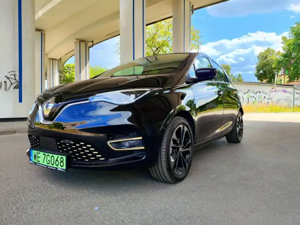 Czarny Renault Zoe błyszczy pod betonowym wiaduktem. Ten elektryczny samochód oferuje imponujący zasięg, idealny na miejskie podróże i dalsze wyprawy.