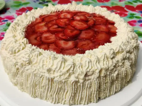 En vacker jordgubbstårta med fluffigt gräddtäcke och ett glansigt jordgubbslager i mitten. Denna ser ut att vara den godaste jordgubbstårtan!
