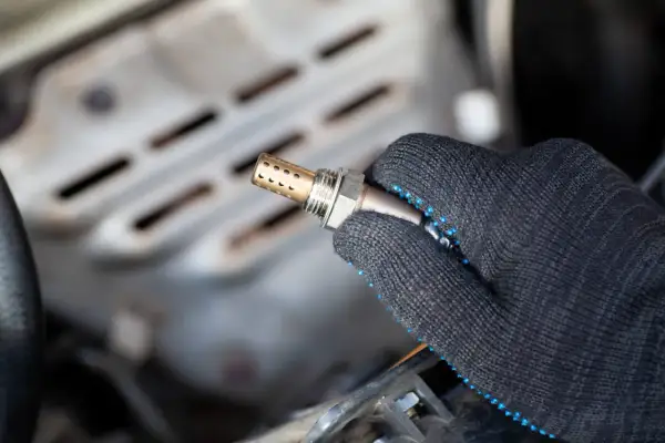 Hand in a glove holds a new auto lambdasonde, ready for installation in a car engine.