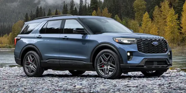 Niebieski Ford Explorer ST na kamienistej plaży, z jesiennym lasem w tle.