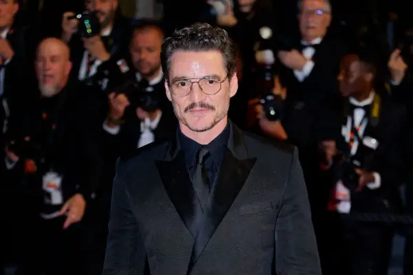 Pedro Pascal sfoggia un impeccabile outfit giacca nera uomo, con camicia e cravatta abbinate, occhiali da vista e baffi.