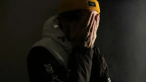 Ein Mann mit gelber Mütze verdeckt sein Gesicht mit den Händen, als ob er mit seinem Gewissen ringt.