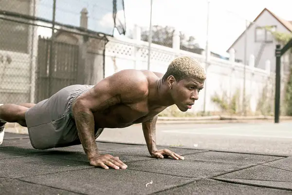 Un homme musclé s'entraîne en extérieur, effectuant des pompes dans un style calisthenics militaire.