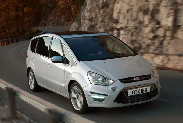 Biały Ford S-Max 2.0 TDCI na krętej drodze wśród jesiennych drzew i skał.