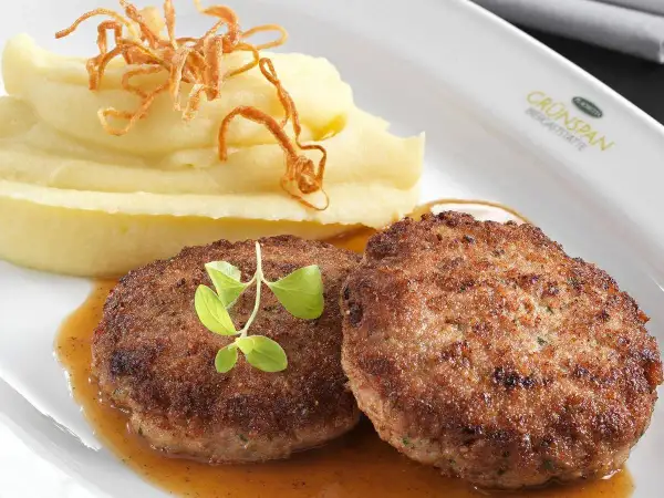 Zwei saftige faschierte Laibchen mit cremigem Kartoffelpüree und knusprigen Röstzwiebeln, garniert mit frischen Kräutern.