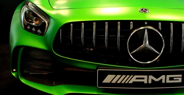 Zielony Mercedes AMG z błyszczącym chromem na grillu i emblematach.