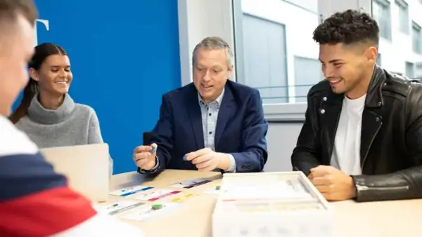 Ein Mann erklärt jungen Leuten beim dualen Studium Marketing Berlin ein Spiel.