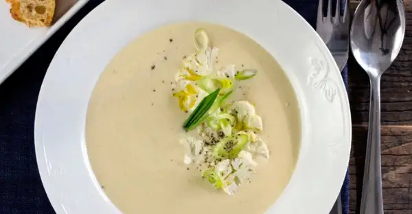 Krämig potatis och blomkålssoppa med garnering av blomkål, salladslök och peppar. Serveras med en bit rostat bröd.