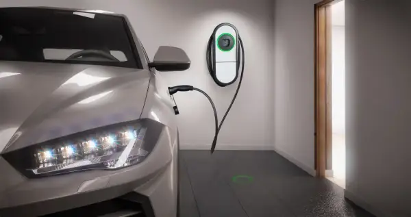 Auto elettrica in ricarica in un box privato. Stazione di ricarica a muro e cavo collegato. Luce verde sul pavimento indica la posizione.
