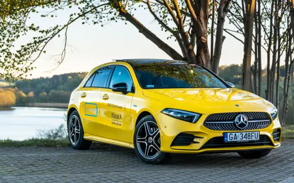 Żółty Mercedes A250 z czarnym dachem i felgami, zaparkowany nad jeziorem.