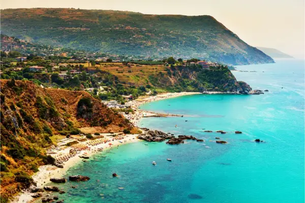 Vista mozzafiato del capo Vaticano a Tropea, con il mare cristallino che lambisce le spiagge affollate e le scogliere verdi.