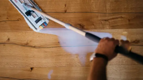 Mano che pulisce un pavimento in legno non trattato con uno straccio umido.