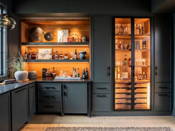 Stylish basement bar ideas featuring illuminated shelves stocked with liquor bottles, glassware, and decorative items.
