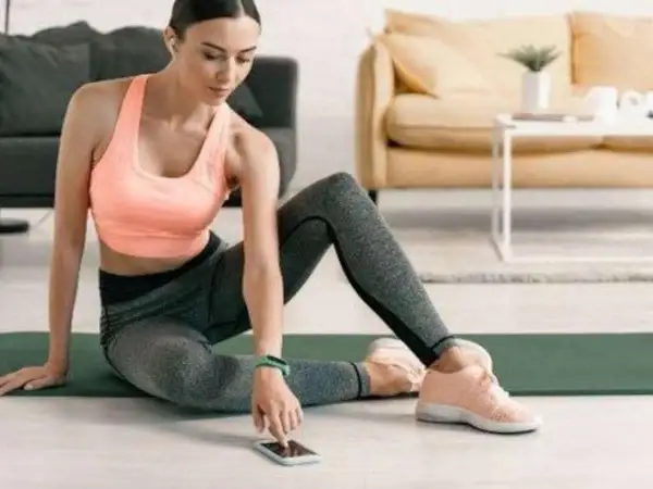 Frau in Sportkleidung sitzt auf einer Matte und bedient ihr Smartphone.