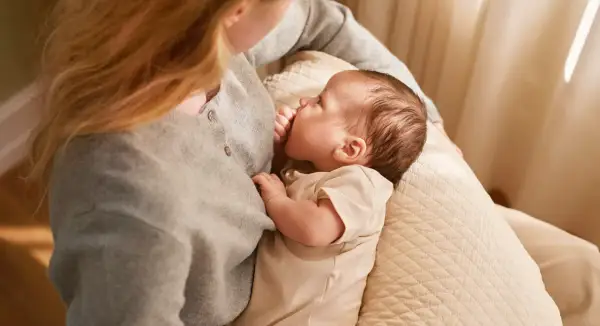 En mamma ammar sin bebis, som är cirka 6 veckor gammal. Mjukt ljus faller in från sidan.