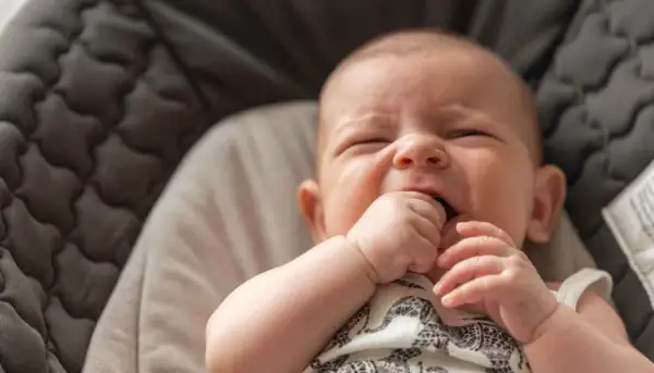 Un bebé de 3 meses no duerme, con los ojos cerrados y la mano en la boca, en una hamaca acolchada.