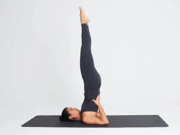 Mujer en postura de yoga invertida. Considera las contraindicaciones de las posturas invertidas en yoga antes de practicar.
