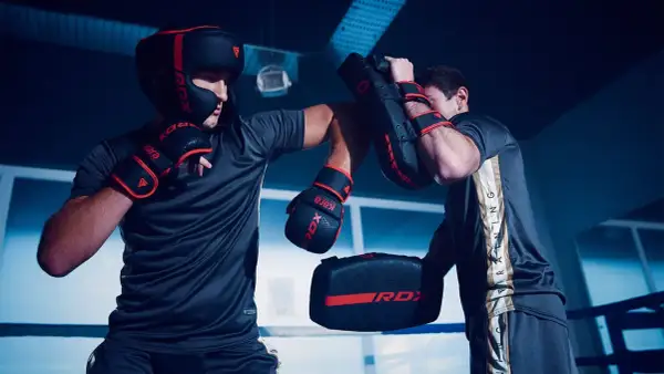Two boxers in a ring, one wearing a headguard and gloves, practicing sparring with pads.