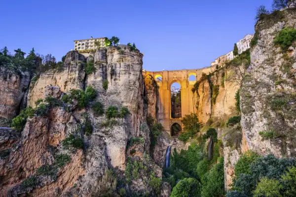 El Puente Nuevo de la Ronda, Málaga, se alza majestuoso sobre un profundo tajo, con cascadas y vegetación adornando sus acantilados.