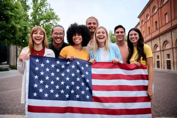 Grupo de jóvenes sonriendo y sosteniendo la bandera de EE.UU. ¡Un año de intercambio en Estados Unidos lleno de alegría!