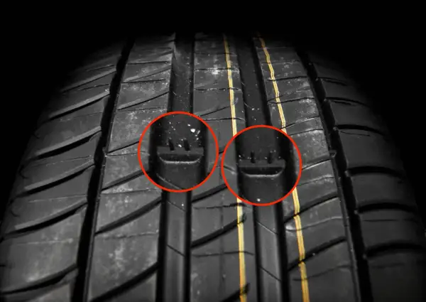 Gros plan sur un pneu de voiture, avec deux cercles rouges mettant en évidence les indicateurs d'usure. C'est un bon indice pour savoir quand changer ses pneus.