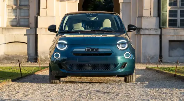 Nowy Fiat 500 w kolorze głębokiej zieleni, z charakterystycznymi okrągłymi światłami, zaparkowany przed zabytkowym budynkiem. Sprawdź aktualną fiat 500 cena!