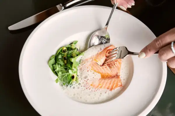 Ein zartes Lachsfilet mit Schaum und Grünzeug auf einem Teller. Ein Genuss in einem Berliner Fischrestaurant.