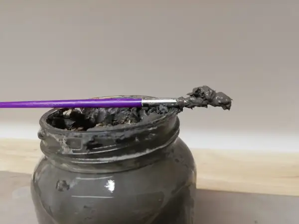 Pinceau violet trempé dans une pâte grise, prête à recoller terre cuite.