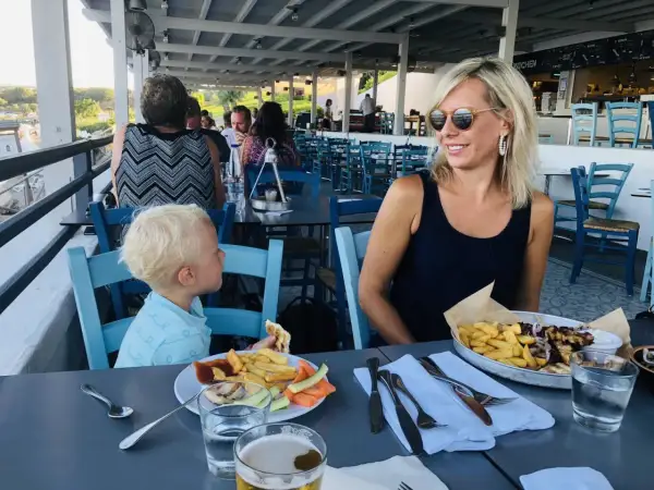 Familj njuter av en måltid på Costas Kitchen Kallithea. En kvinna ler, en pojke äter, och maten ser utsökt ut.