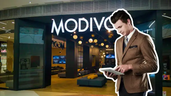 Elegancki mężczyzna w garniturze przegląda tablet przed sklepem MODIVO. W tle widać promocje CCC GPW.